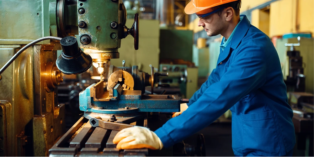 Machinist in hard hat and blue overalls operating a milling machine