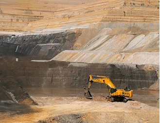 Yellow excavator working at the base of a terraced open-pit mine wall