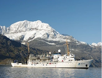 White research ship anchored near a snow-capped mountain