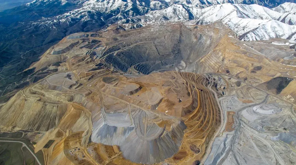 Aerial view of a large terraced open-pit mine with snow-capped mountains behind