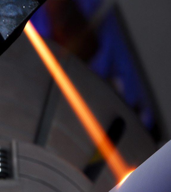Blurred orange thermal spray stream striking a metal surface in a dark workshop