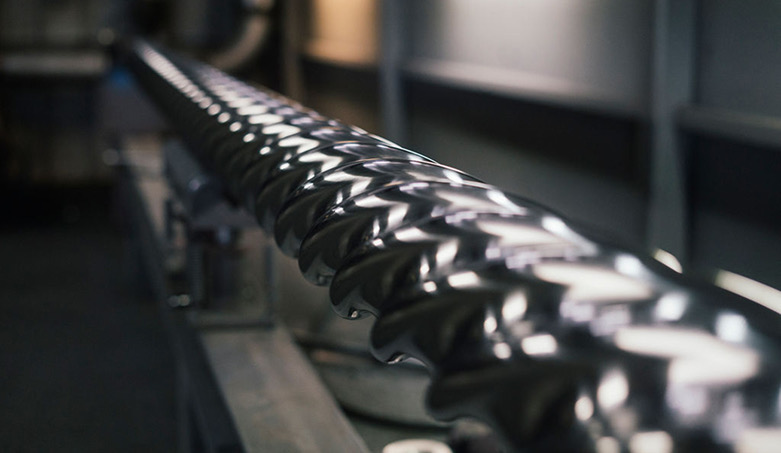 Polished helical shaft with reflective spiral grooves lying on a machine bed