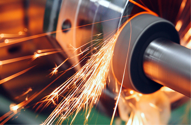 Grinding wheel throwing orange sparks while machining a steel cylindrical shaft