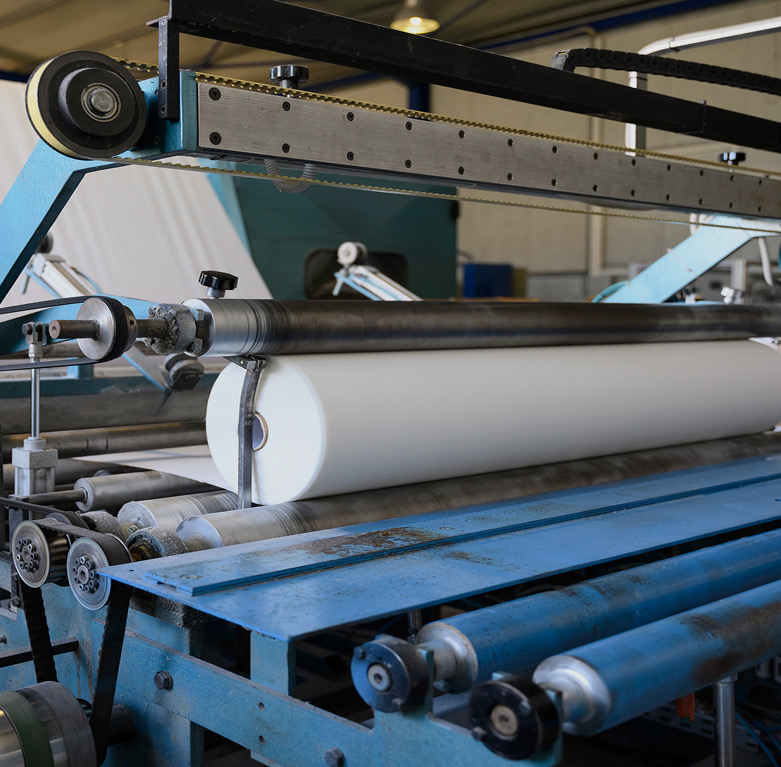 Industrial roller machine feeding a large roll of white material over steel rollers